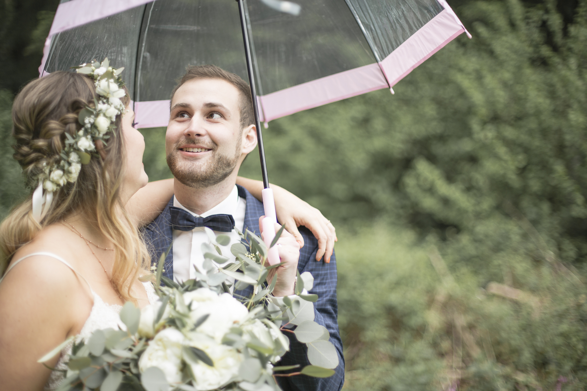 Braut und Bräutigam strahlend bei Regen unter dem Schirm.