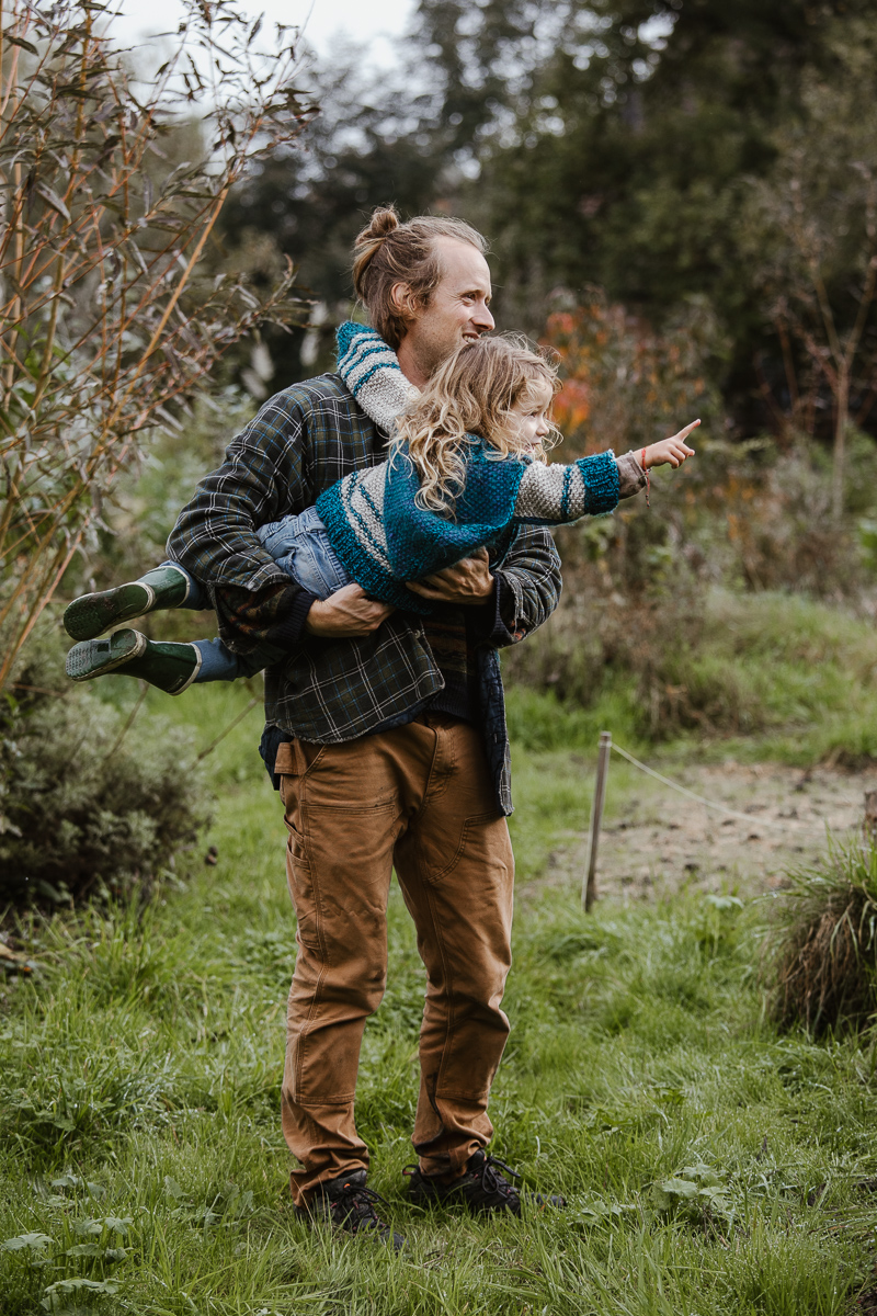 Lucas hält seine Tochter. Sie zeigt in die Ferne über die Permakulturanlage.
