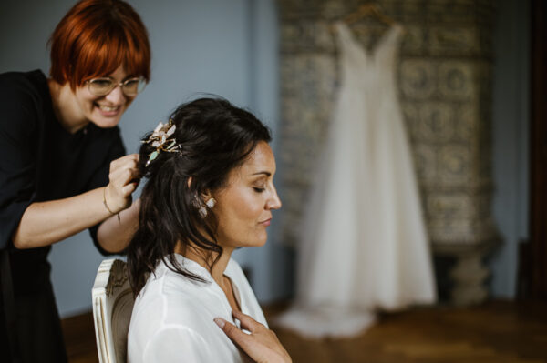 Braut wird für ihre Freie Trauung frisiert. Im Hintergrund das Brautkleid am Kachelofen des Blauen Zimmers im Schlössli Utenberg.