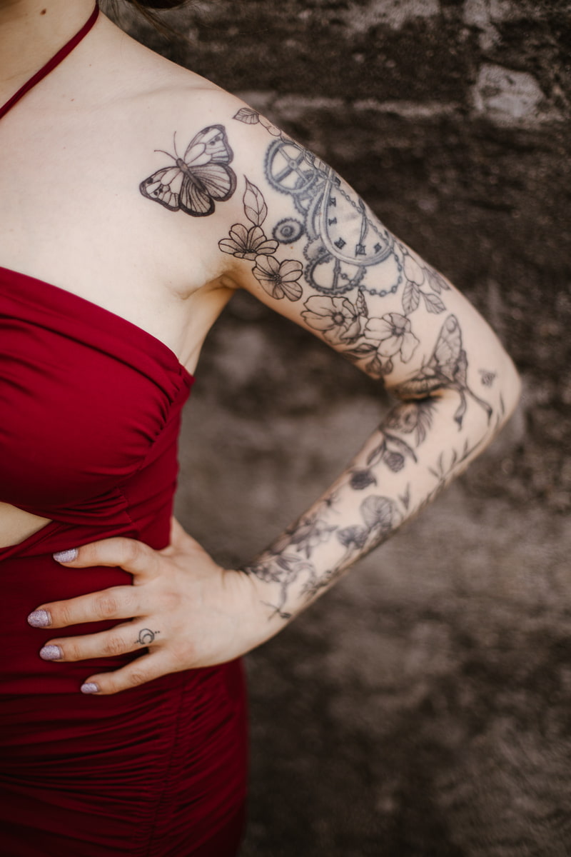 Detailaufnahme des Arm-Tattoos der Frau mit Schmetterlings- und Blumenmotiv im roten Kleid